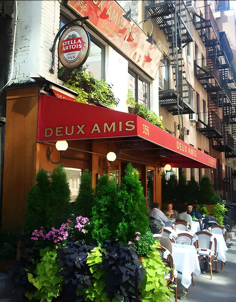 Red awning and sidewalk tables with planters outside a brick corner storefront