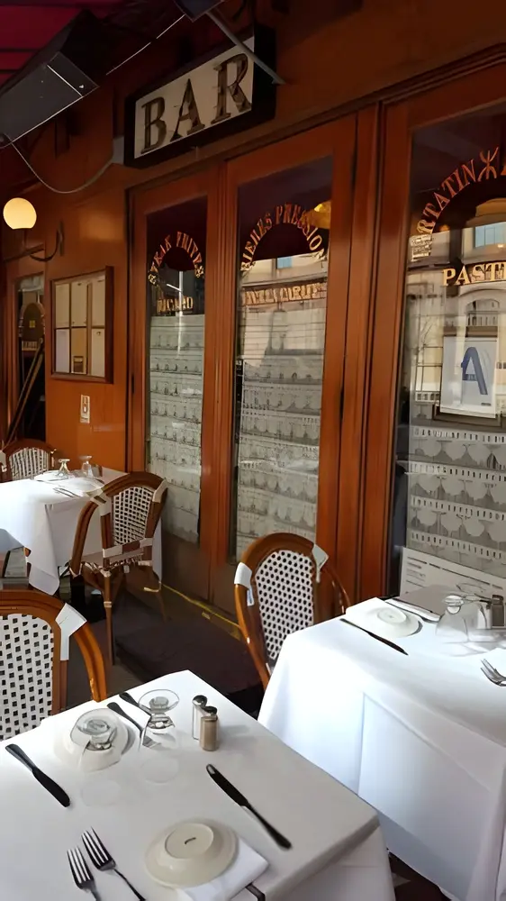 White-clothed tables and wicker bistro chairs beside glass doors under a bar sign
