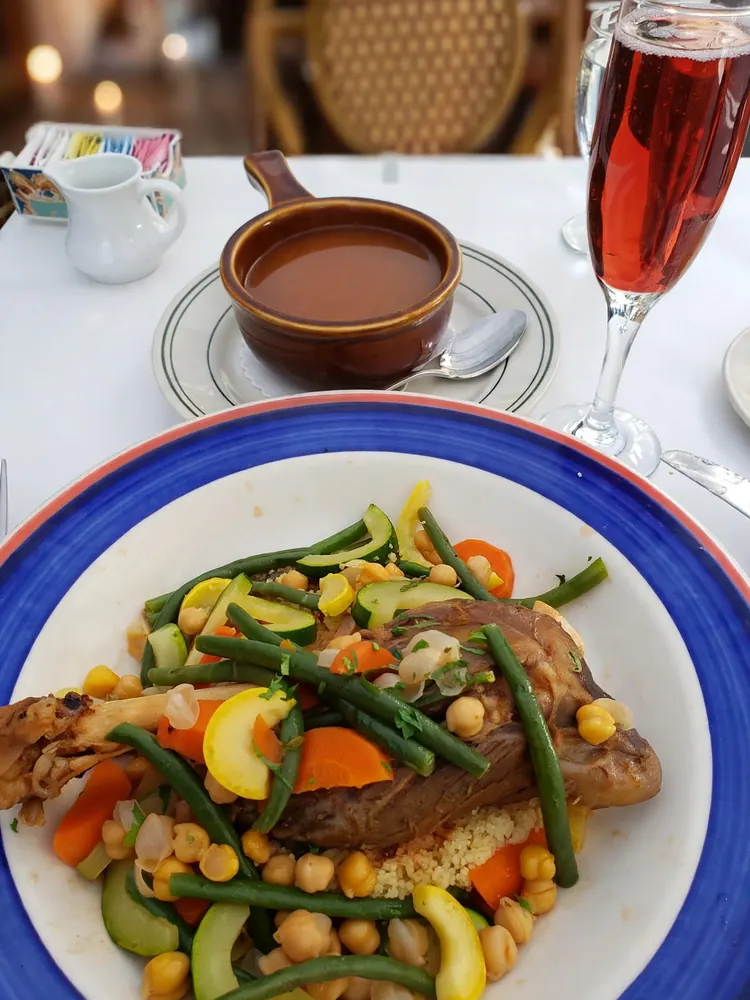 Blue-rimmed plate of braised meat with green beans and chickpeas, beside a glass of rosé