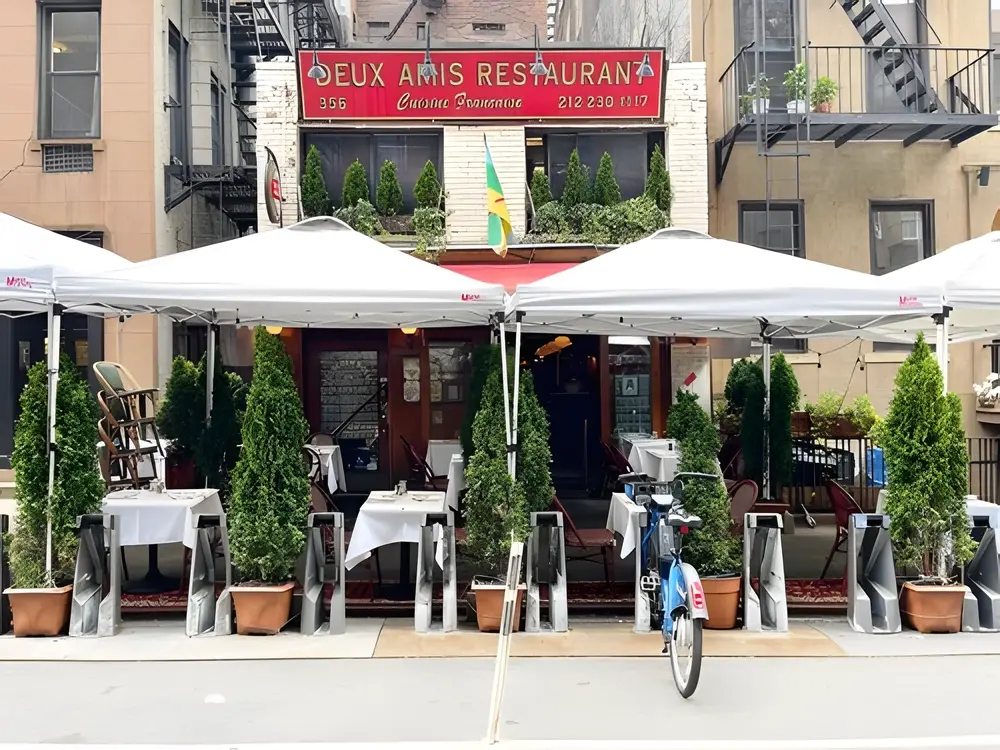 Sidewalk tables under white umbrellas in front of a red-signed brick restaurant