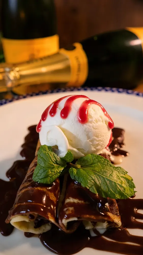 Chocolate-drizzled crêpes topped with ice cream, raspberry sauce and mint, with champagne bottles behind