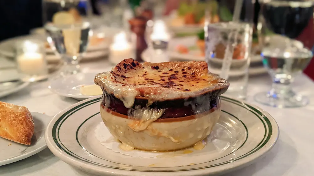 Onion soup with browned melted cheese crust in a crock beside a piece of bread