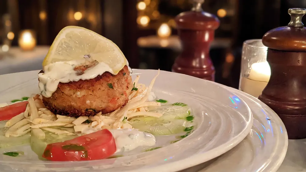 Crab cake with lemon wedge, tomato slices and slaw on a white plate