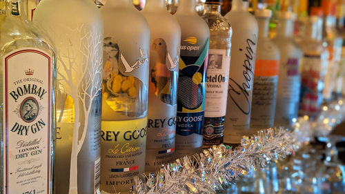 Gin and vodka bottles lined up on a shelf with silver tinsel