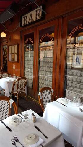 White-clothed tables and wicker bistro chairs beside glass doors under a bar sign