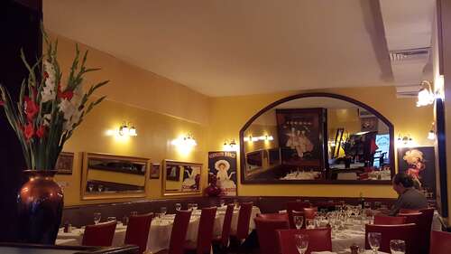 Dining room with yellow walls, arched mirror, vintage posters and tables set with white linens