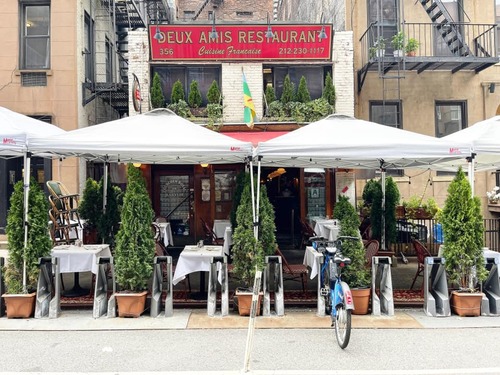 Sidewalk tables under white umbrellas in front of a red-signed brick restaurant