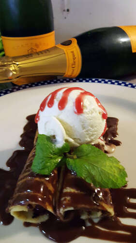 Chocolate-drizzled crêpes topped with ice cream, raspberry sauce and mint, with champagne bottles behind