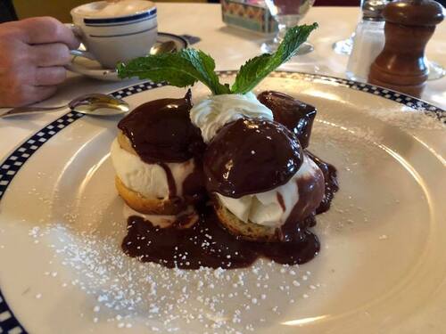 Cream puffs covered in chocolate sauce with whipped cream, powdered sugar and a mint sprig