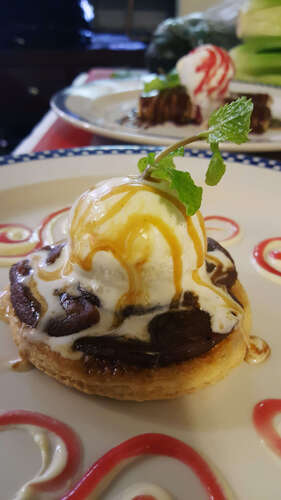 Scoop of vanilla ice cream with caramel and mint on a chocolate pastry round