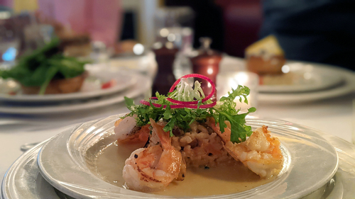 Seared shrimp over rice with a frisée garnish in a shallow white bowl