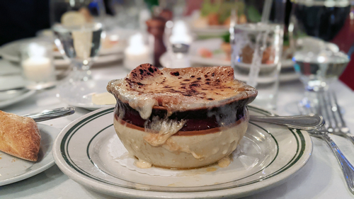 Onion soup with browned melted cheese crust in a crock beside a piece of bread