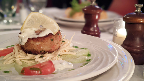 Crab cake with lemon wedge, tomato slices and slaw on a white plate
